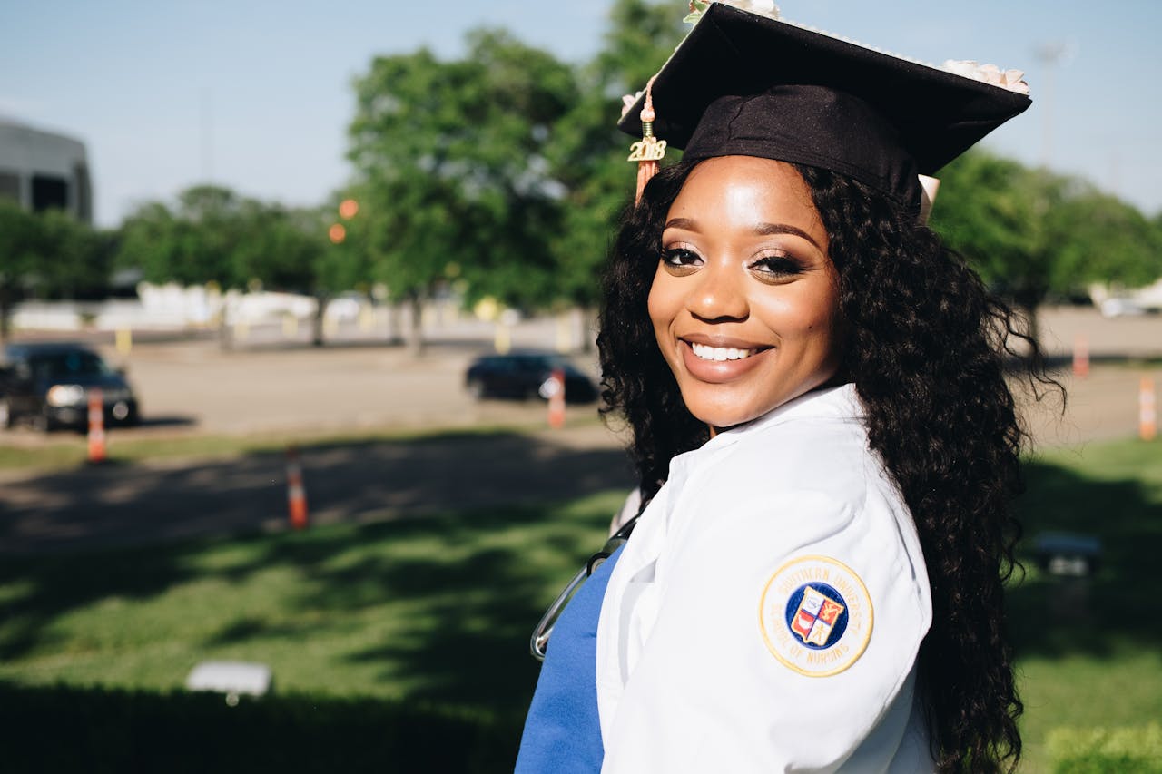 African American woman in graduation attire, smiling outdoors, symbolizing academic success.
