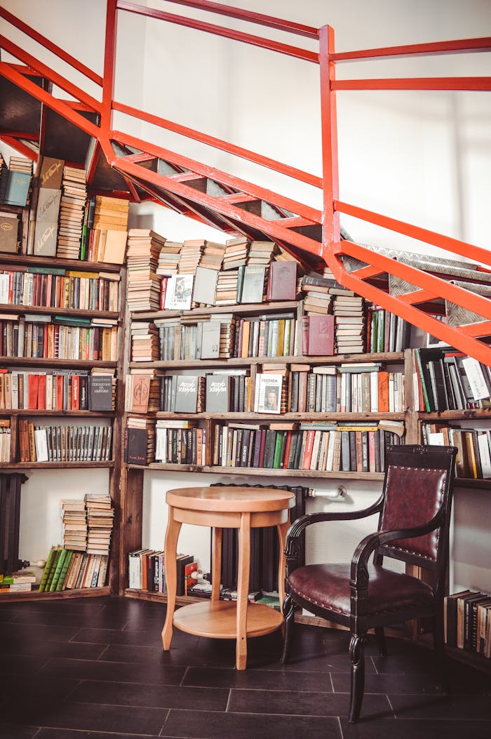 A cozy library corner featuring bookshelves, a wooden chair, and red stairs inside a modern interior.