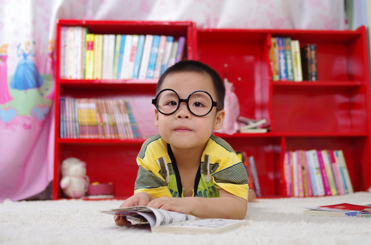 services-01 A cute child in glasses reading a book, surrounded by colorful shelves. Perfect shot of childhood learning indoors.