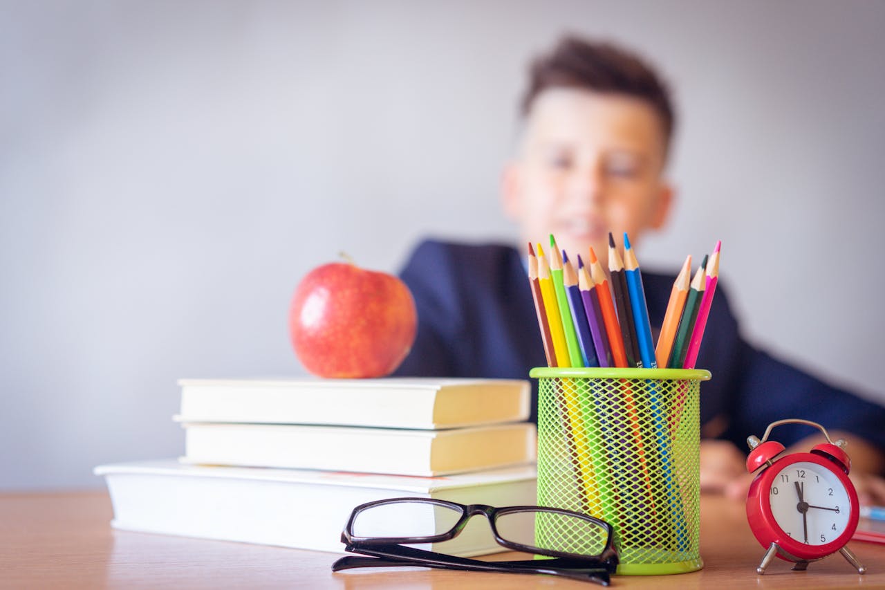 hero-img Schoolboy smiling behind a desk with books, pencils, and an alarm clock symbolizing study and creativity.